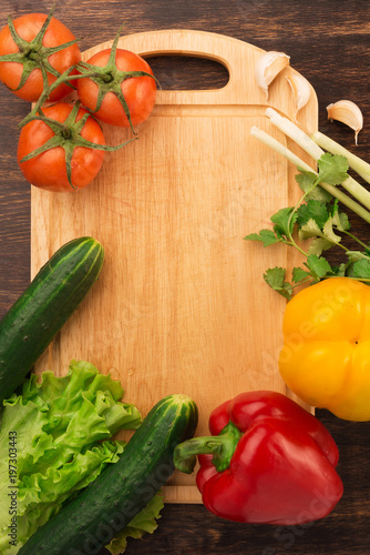 Various vegetables and empty cutting board. Colorful ingredients for cooking on rustic wooden table around empty cutting board with copyspace. Top view.