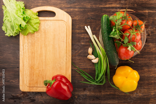 Various vegetables and empty cutting board. Colorful ingredients for cooking on rustic wooden table around empty cutting board with copyspace. Top view.