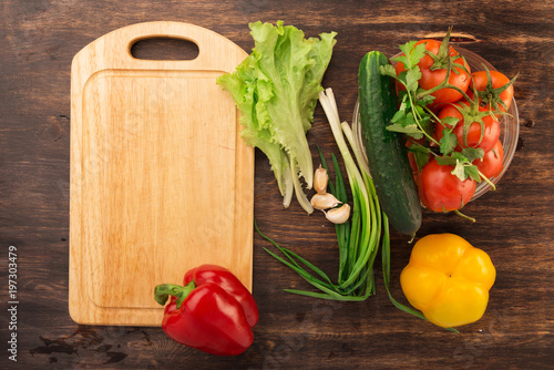 Various vegetables and empty cutting board. Colorful ingredients for cooking on rustic wooden table around empty cutting board with copyspace. Top view.