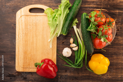 Various vegetables and empty cutting board. Colorful ingredients for cooking on rustic wooden table around empty cutting board with copyspace. Top view.