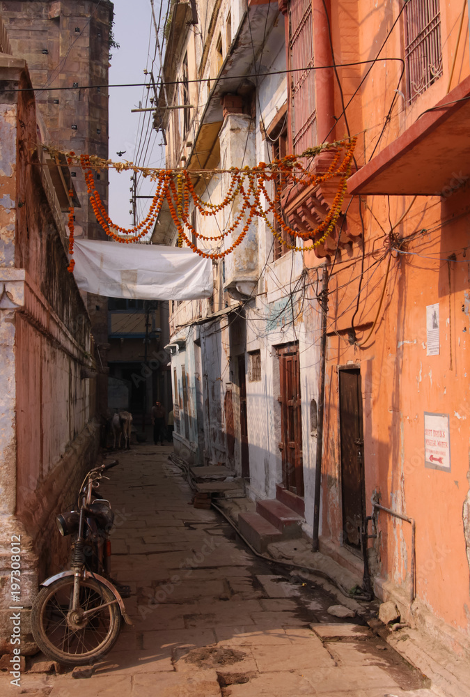 Colorful city view of narrow ancient street in Varanasi with authentic indian atmosphere and old bike parked on the corner in the foreground. State Uttar Pradesh, India.