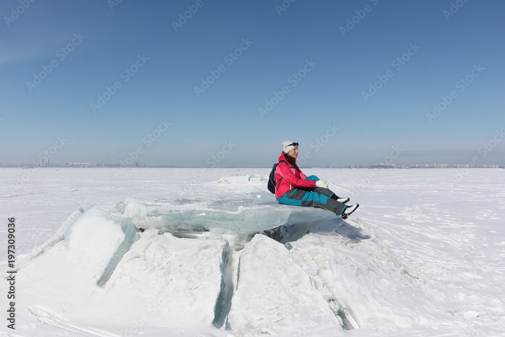 Happy woman in a red jacket sitting on an ice floe on a frozen river, Ob reservoir, Russia