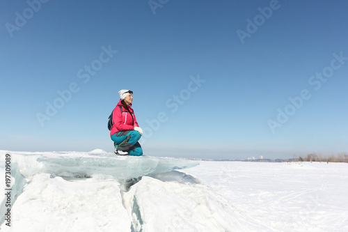 Happy woman in a red jacket sitting on an ice floe on a frozen river, Ob reservoir, Russia