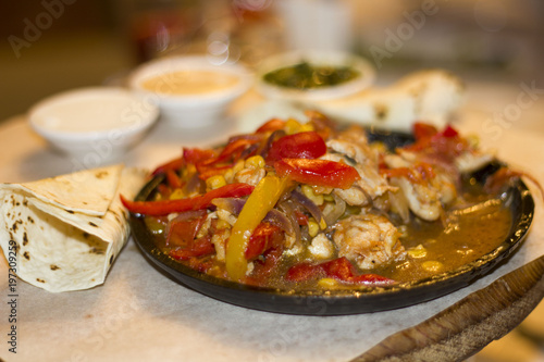 pieces of meat with onion pepper corn on a frying pan and sauces on the table