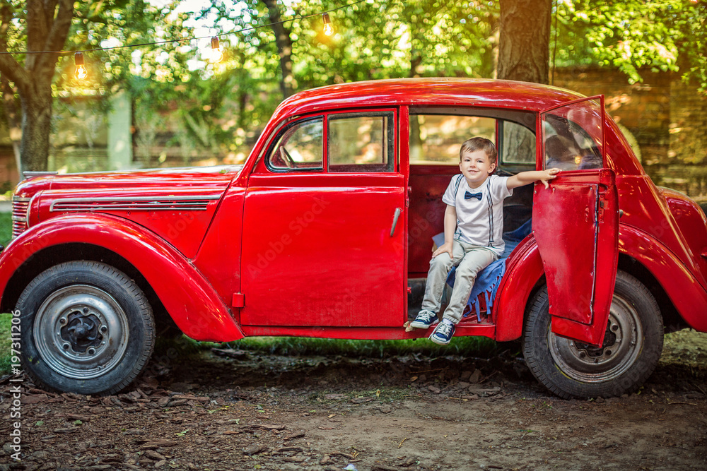 Cute little boy in a bow tie is sitting in an old red car Cute little boy in a bow tie is sitting in an old red car