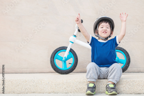 Closeup happy kid with smile face sit on marble stone floor with bicycle onstone wall textured background with copy space photo