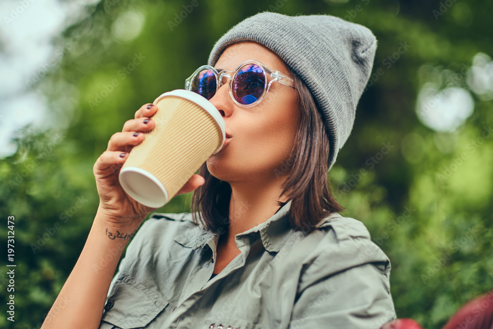 A hipster woman in hat sitting on a bench in a city park. Relaxing in nature. A hipster woman in hat sitting on a bench in a city park. Relaxing in nature.
