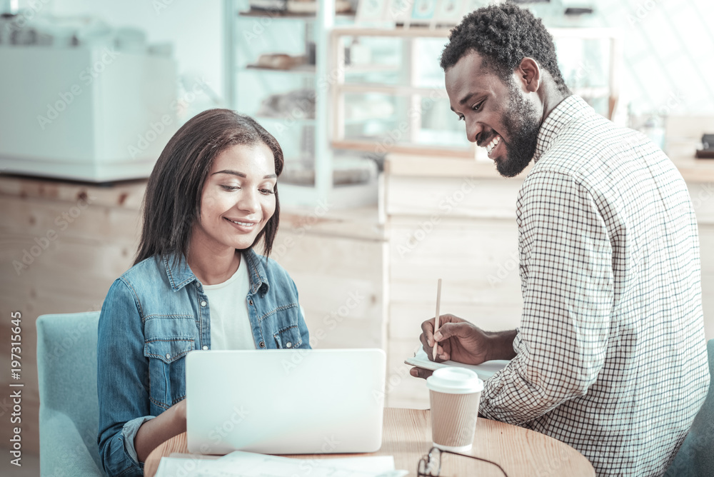 Modern device. Positive nice joyful woman smiling and looking at the netbook screen while studying together with his friend