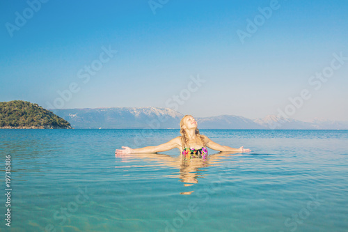 Young woman enjoying warm sunrise light, breathing fresh air and feeling the freedom in Adriatic sea beside mountains in Croatia in summer. Blue sky in the morning. Peaceful atmosphere. 