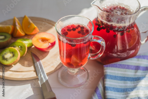 Compote of red berries in a pitcher and a glass, fresh fruit on a rustic table