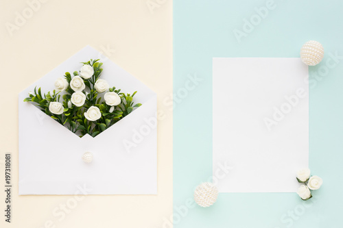Workspace. Wedding invitation card, envelope, white roses and green leaves on beige blue background. Overhead view. Flat lay, top view wedding invitation card Templates.