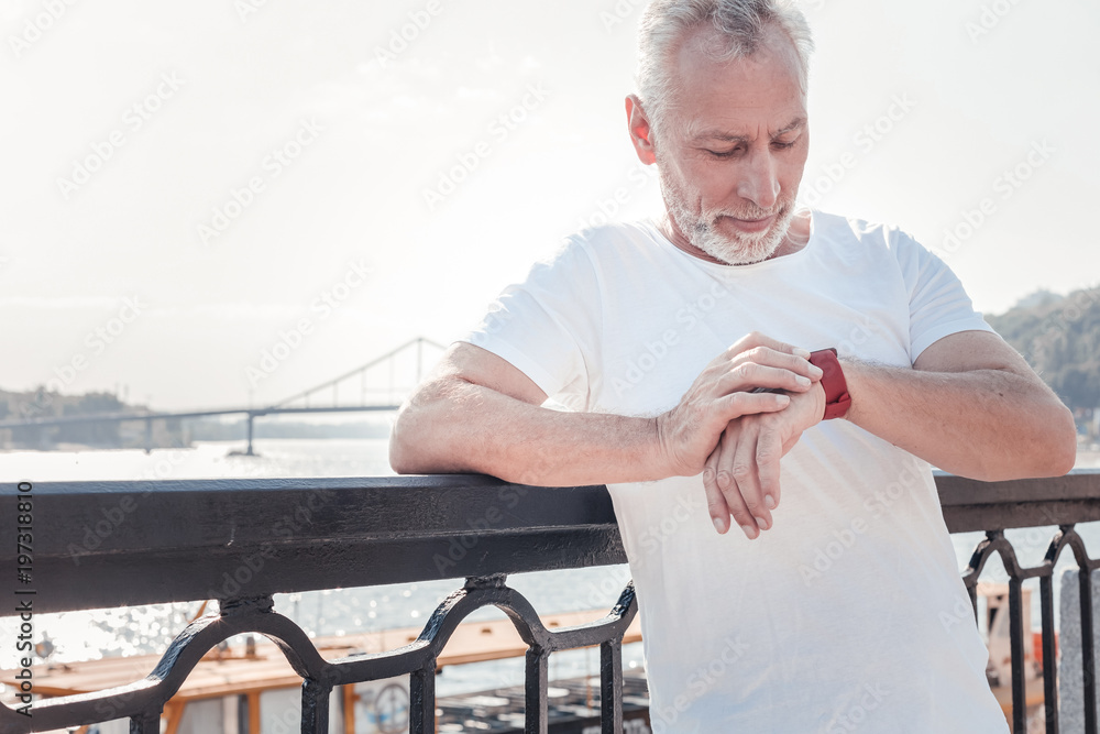 What time is it. Smart aged handsome man standing on the quay leaning to the railing and looking at his watch. What time is it. Smart aged handsome man standing on the quay leaning to the railing and looking at his watch.