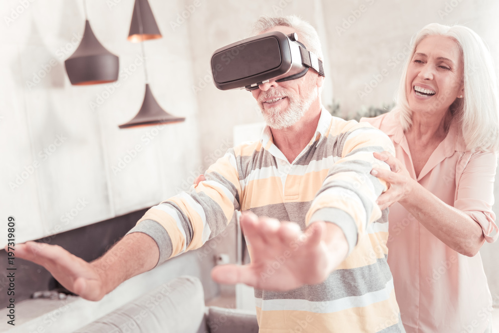 Be careful. Joyful aged interested man standing in the bright room holding hands in front of himself and using the gadget. Be careful. Joyful aged interested man standing in the bright room holding hands in front of himself and using the gadget.
