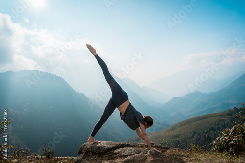 Sporty woman practicing yoga on mountain cliff at sunrise. Healthy lifestyle.