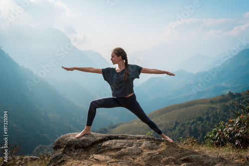 Woman doing yoga on mountain cliff at sunrise. Mountanious landscape