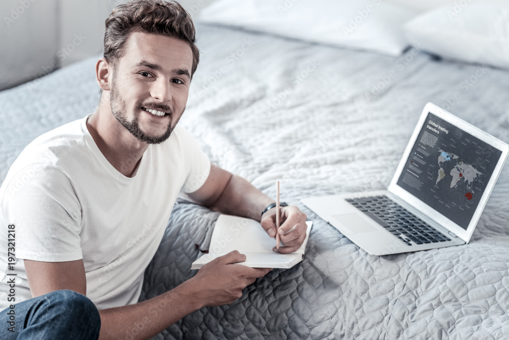 For notes. Nice positive cheerful man holding his notebook and smiling while looking at you