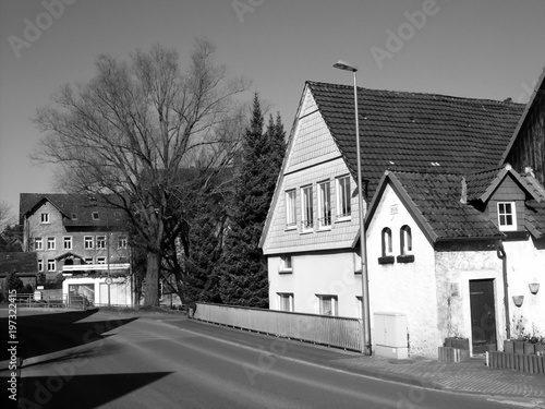 Dorfstraße im Winter bei Sonnenschein in Heidenoldendorf bei Detmold am Teutoburger Wald in Ostwestfalen-Lippe, fotografiert in neorealistischem Schwarzweiß