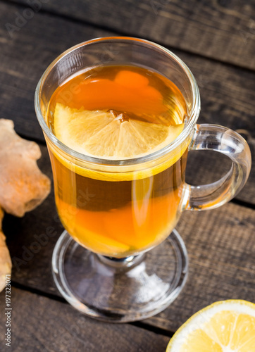 A cup of ginger tea with lemon on a wooden background.