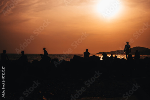 silhouettes of people resting on beach by the sea against sunset