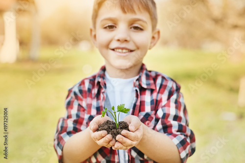 Rich vertility. Close up of a cheerful little boy holding handful of soil and smiling while standing in the garden