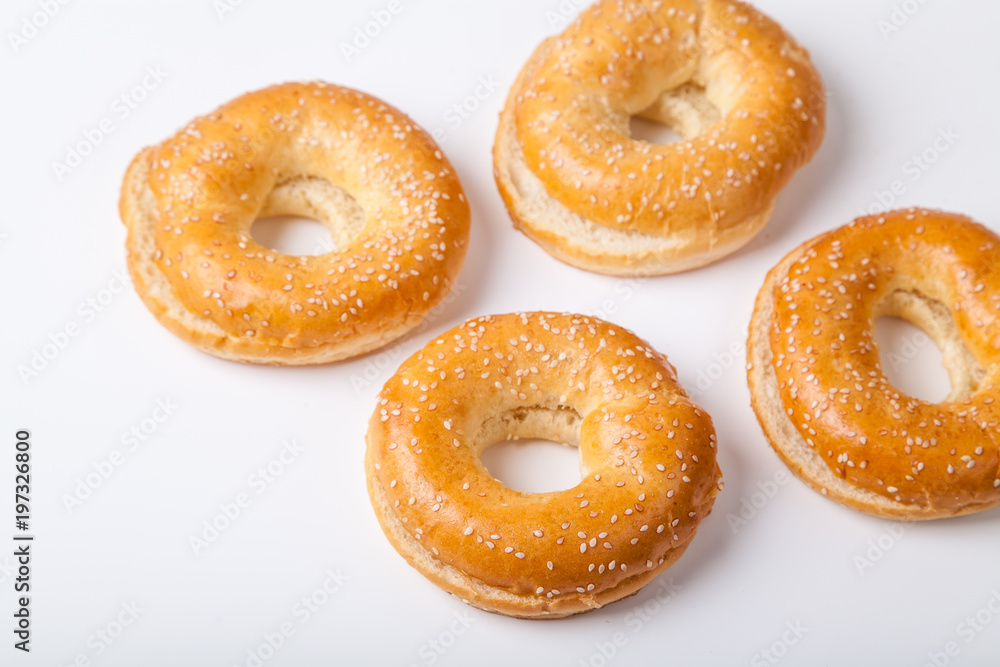 Four fresh baked bagle buns with sesame seeds on white background pre-cut for making sandwiches