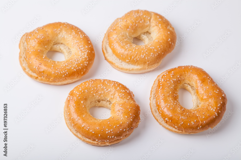 Four fresh baked bagle buns with sesame seeds on white background pre-cut for making sandwiches