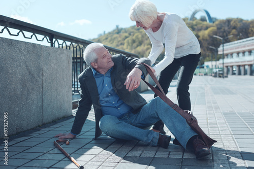 Real example of humanity. Smiling lady holding a hand of a poor man and helping him after falling down in the street.