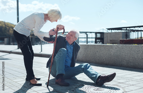 Let me help you. Loving wife giving her husband to lean on her after falling to the ground during a daily promenade.