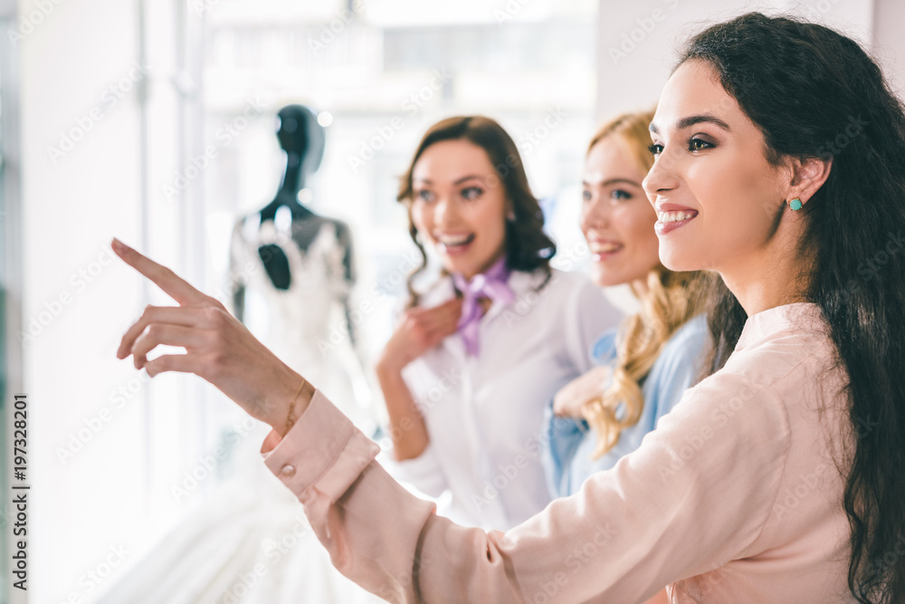 Young smiling bride and bridesmaids choosing dresses in wedding fashion shop Young smiling bride and bridesmaids choosing dresses in wedding fashion shop