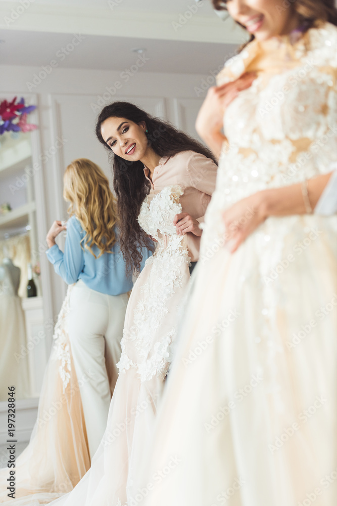 Young smiling bride and bridesmaids choosing dresses in wedding fashion shop