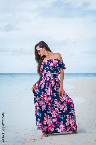 Woman in long dress on beach with pure water of ocean in Maldives