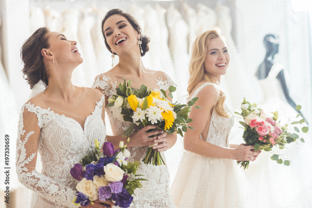 Happy women in wedding dresses with flowers in wedding atelier Happy women in wedding dresses with flowers in wedding atelier