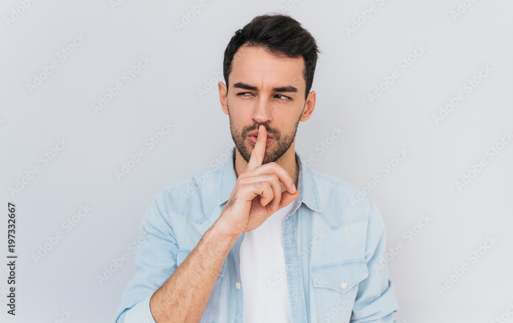 Portrait of serious fashionable male dressed trendy in blue shirt, keeps fore finger on lips, making shh gesture for secret or be quiet. Isolated shot of stylish man shows silence sign. People concept Portrait of serious fashionable male dressed trendy in blue shirt, keeps fore finger on lips, making shh gesture for secret or be quiet. Isolated shot of stylish man shows silence sign. People concept