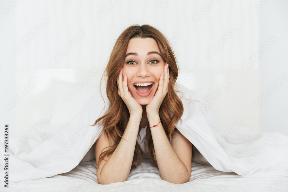 Portrait of a happy young woman lying in bed