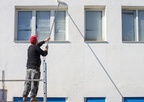 Imbianchino dipinge di bianco  una facciata di uno stabile