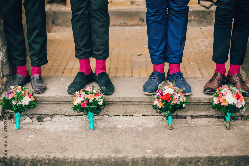 Men's feet in stylish shoes and bright socks. Groomsmen shoes and socks near wedding flowers bouquet.