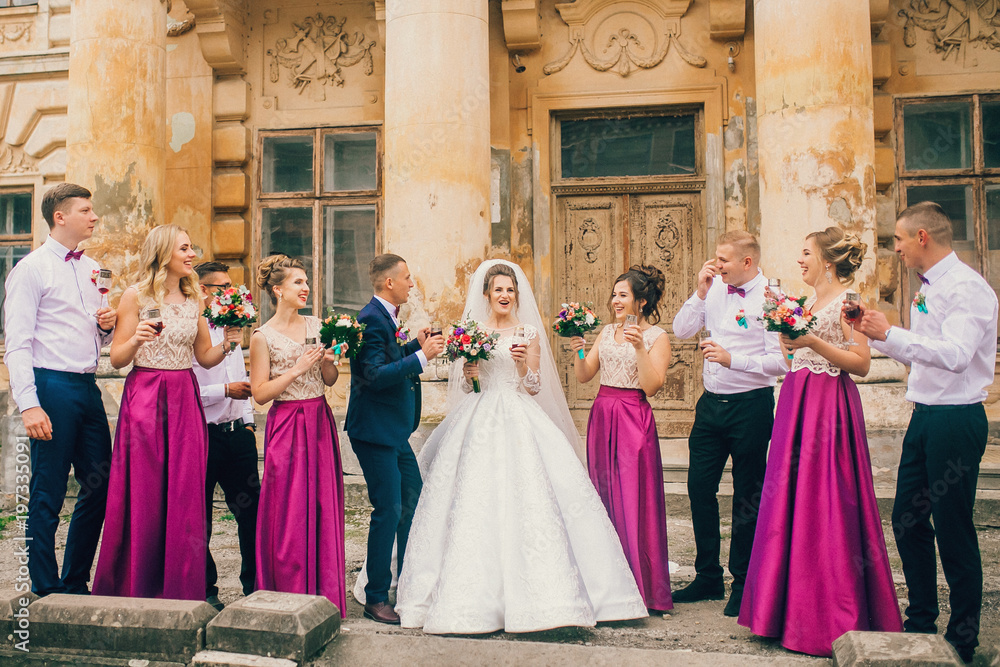 Couple of newlyweds, bride and groom together with bridesmaids and groomsmen drinking champagne outdoors hands closeup, wedding celebration with friends . 