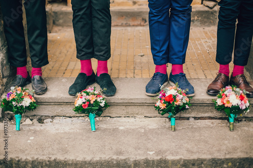 Obraz na płótnie Men's feet in stylish shoes and bright socks. Groomsmen shoes and socks near wedding flowers bouquet. w salonie
