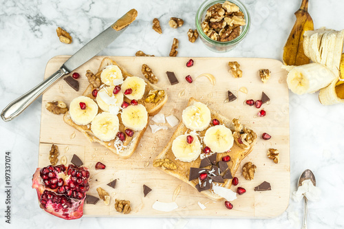 Sandwich with peanut butter, banana slices and chocolate on wooden cutting board