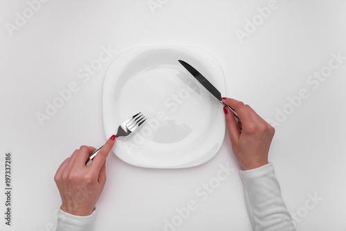 Hands with cutlery over empty plate.