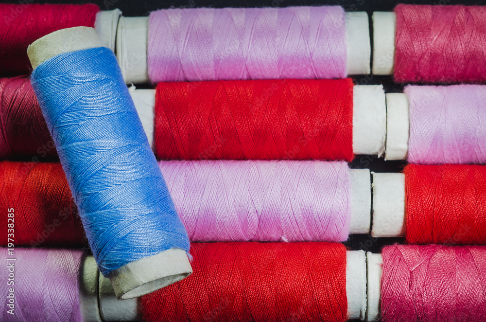 Spool of blue thread on the background of spools of pink and red thread Spool of blue thread on the background of spools of pink and red thread