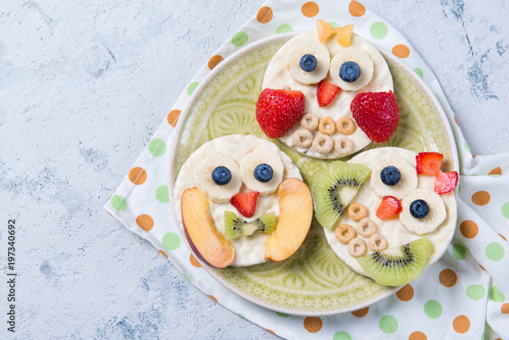 Obraz premium Rice cakes with yoghurt and fresh fruits in a shape of cute owls on a plate, meal for kids idea, top view
