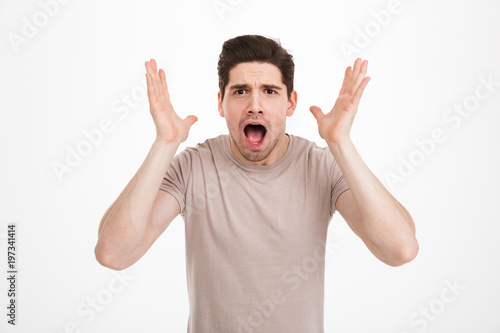 Photo of frustrated man 30s yelling and lifting hands in anger or disappointment, isolated over white background