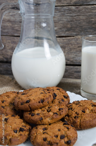 Oatmeal chocolate chip cookies  jug and glass of milk  rustic wooden background.