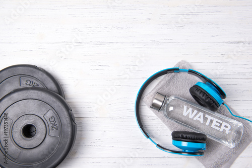 Fitness concept, bottle of water, weight plates and blue headphones on wooden background, top view
