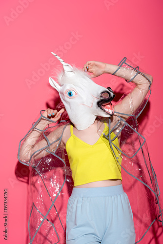 Vászonkép ridiculous woman in fashionable transparent raincoat and unicorn mask on red