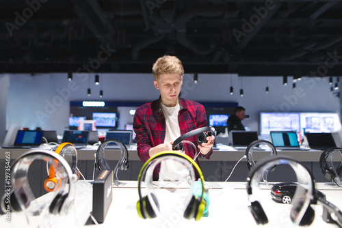 Young man looks at headphones in the electronics store Choosing and buying headphones in a technology store. photo