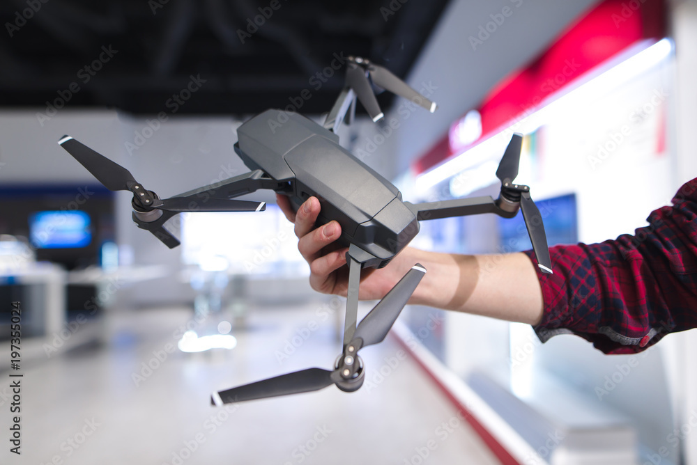 A man's hand holds a quadcopter in the background of a electronics store. Purchase a dron in a hardware store A man's hand holds a quadcopter in the background of a electronics store. Purchase a dron in a hardware store