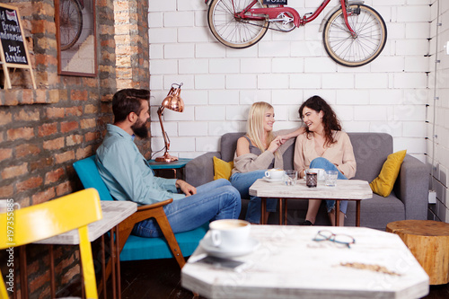 Group of people having a coffee together. Two young women and guy in cafe talking, drinking, laughing and enjoying their time