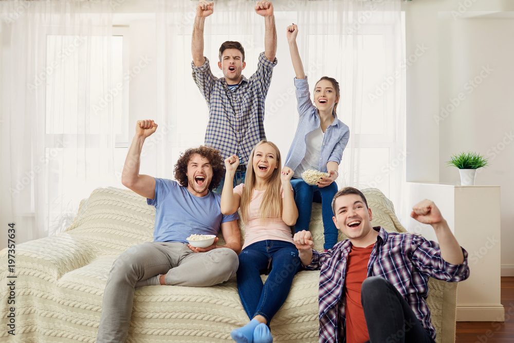 A group of friends of fans watching a sports TV sitting on a sofa in the room. A group of friends of fans watching a sports TV sitting on a sofa in the room.